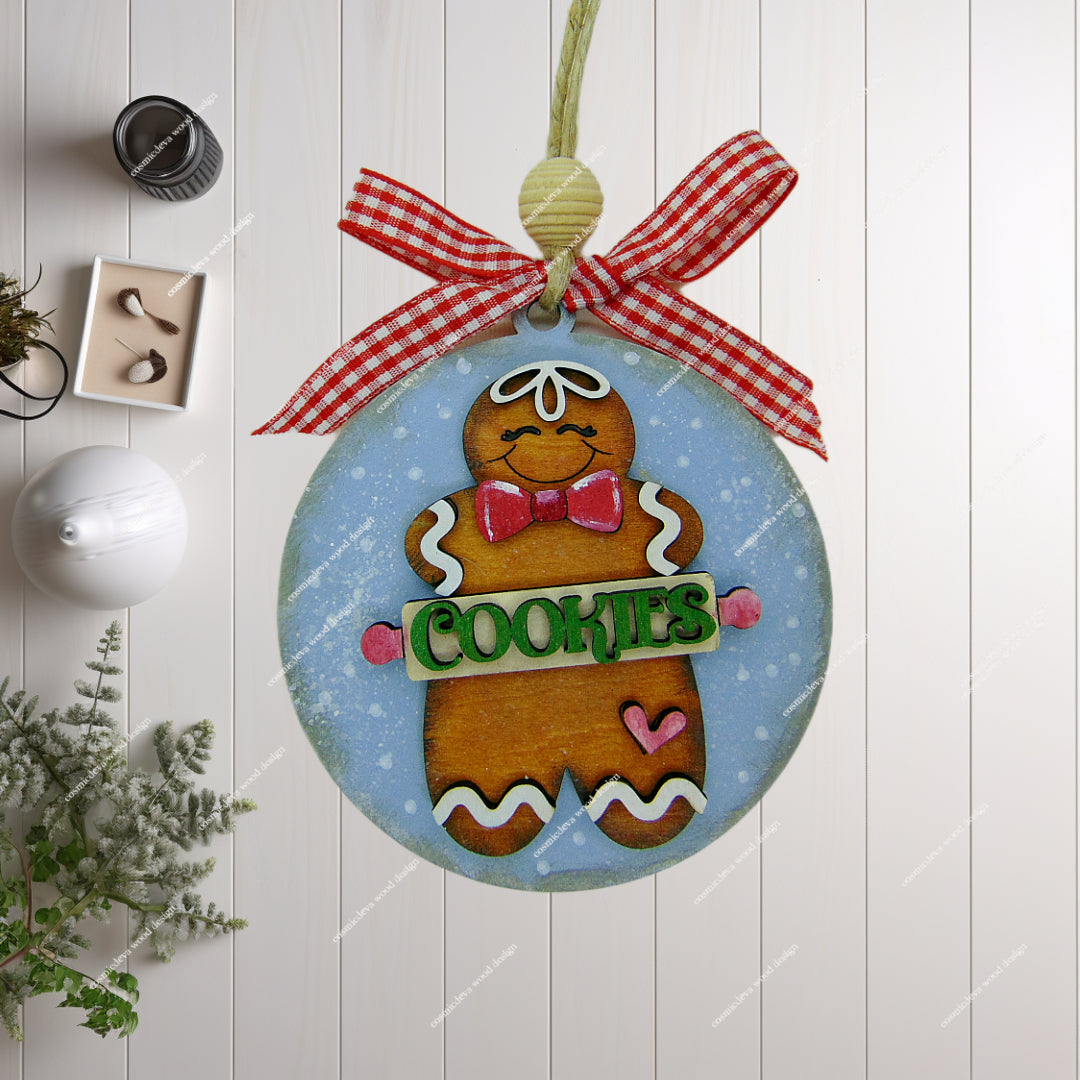 Hand painted wooden gingerbread man Christmas ornament with rolling pin “Cookies” cut out, blue sprinkle background, jute twine, wood bead, and checkered bow. Cute handmade holiday décor for bakers and cookie lovers.
