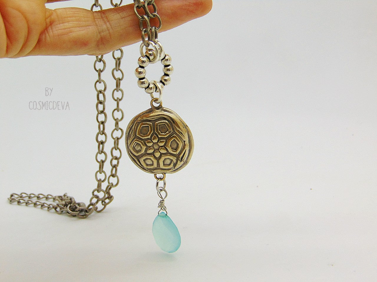 Beautiful handmade silver bronze lentil pendant with a mandala texture and a large faceted briolette aqua blue chalcedony gemstone dangle bead. The large hand formed lentil bead is double sided with two different designs and so can be worn facing either side. The pendant suspends from an 18 inch – 20-inch-long chain with accentual faceted Brazilian aquamarine abacus beads and Tibetan silver beads.