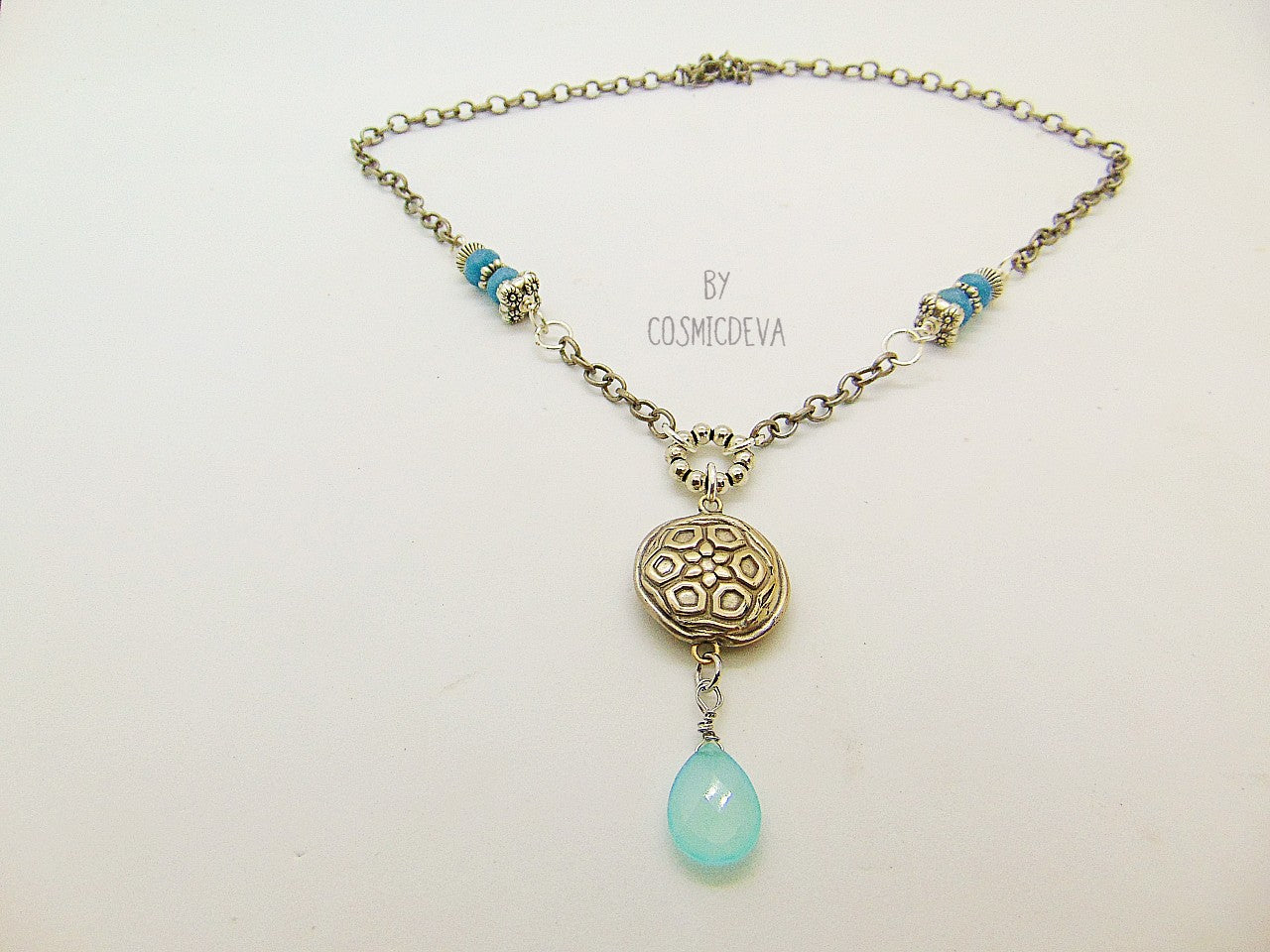 Beautiful handmade silver bronze lentil pendant with a mandala texture and a large faceted briolette aqua blue chalcedony gemstone dangle bead. The large hand formed lentil bead is double sided with two different designs and so can be worn facing either side. The pendant suspends from an 18 inch – 20-inch-long chain with accentual faceted Brazilian aquamarine abacus beads and Tibetan silver beads.