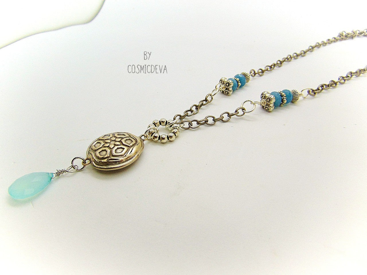 Beautiful handmade silver bronze lentil pendant with a mandala texture and a large faceted briolette aqua blue chalcedony gemstone dangle bead. The large hand formed lentil bead is double sided with two different designs and so can be worn facing either side. The pendant suspends from an 18 inch – 20-inch-long chain with accentual faceted Brazilian aquamarine abacus beads and Tibetan silver beads.
