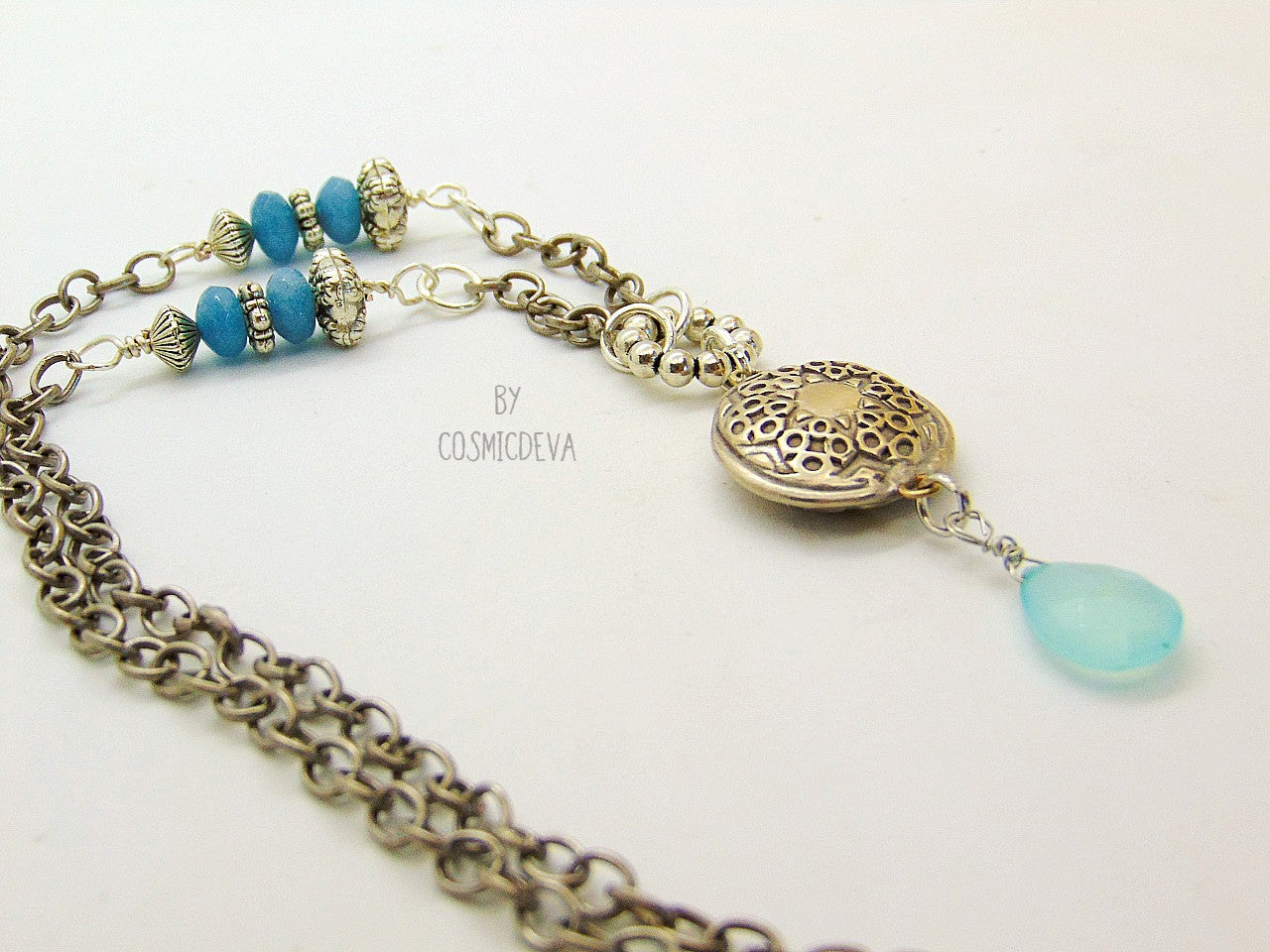 Beautiful handmade silver bronze lentil pendant with a mandala texture and a large faceted briolette aqua blue chalcedony gemstone dangle bead. The large hand formed lentil bead is double sided with two different designs and so can be worn facing either side. The pendant suspends from an 18 inch – 20-inch-long chain with accentual faceted Brazilian aquamarine abacus beads and Tibetan silver beads.