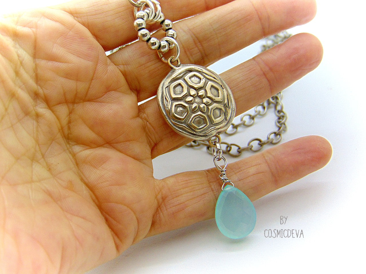 Beautiful handmade silver bronze lentil pendant with a mandala texture and a large faceted briolette aqua blue chalcedony gemstone dangle bead. The large hand formed lentil bead is double sided with two different designs and so can be worn facing either side. The pendant suspends from an 18 inch – 20-inch-long chain with accentual faceted Brazilian aquamarine abacus beads and Tibetan silver beads.