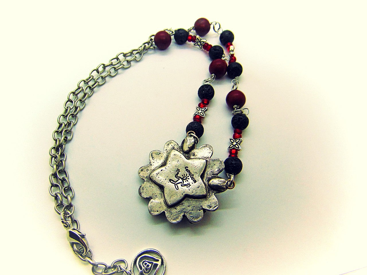 Unique detailed silver bronze Frida Kahlo sugar skull pendant necklace influenced by Mexican culture and symbolism. The flower shaped 3d pendant is featuring a sugar skull decorated with the typical Frida Kahlo signature floral wreath and faceted red garnet cubic zirconia gemstones as eyes. Incorporated flowers, roses, leaves and tiny hearts surrounding the skull. On the backside of the pendant is the CosmicDeva Hallmark