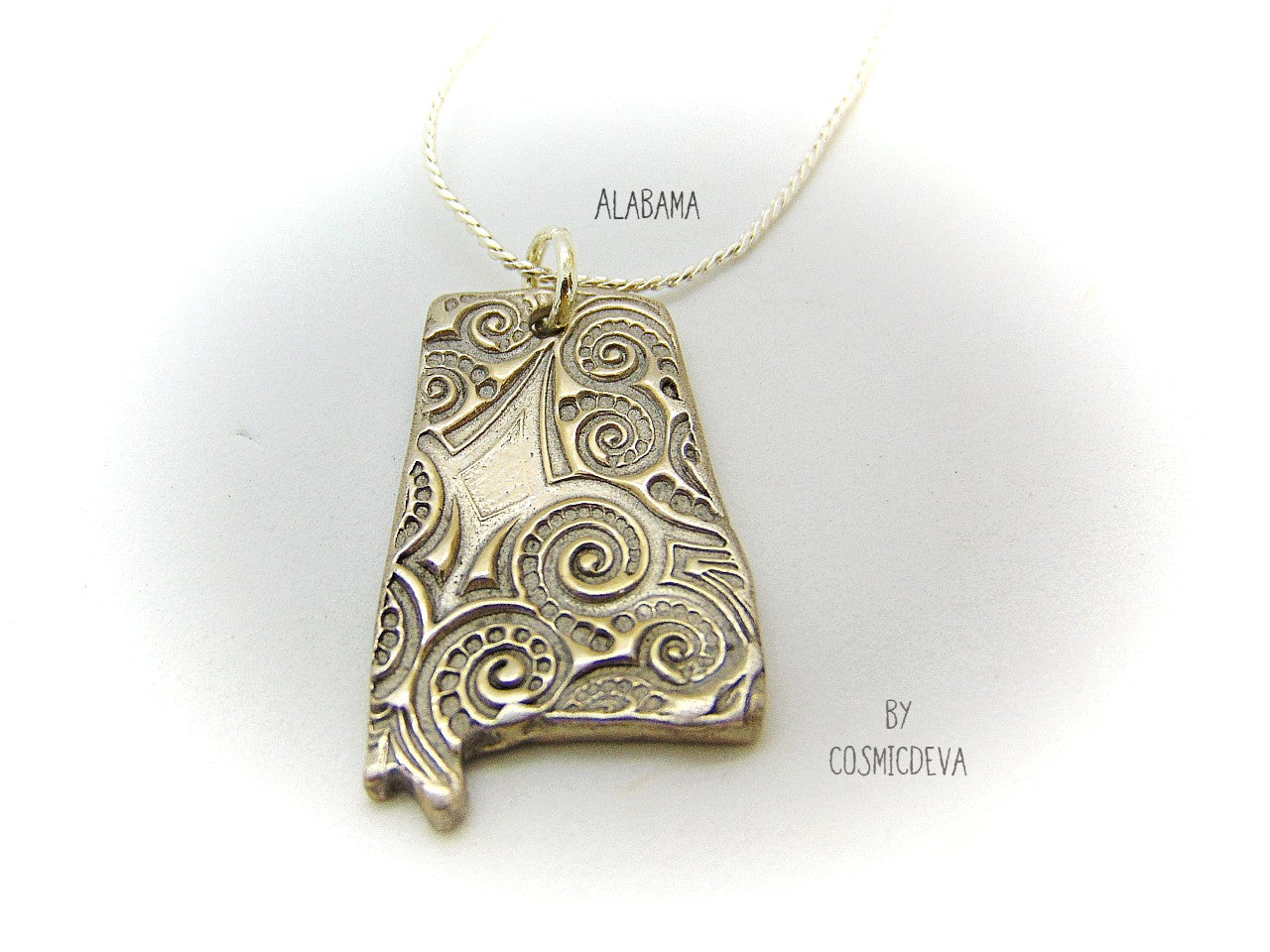 handcrafted and kiln fired Alabama State shaped pendant made of silver bronze. This Alabama pendant dangles from a 20-inch silver plated chain. The backside of the pendant is signed by CosmicDeva.