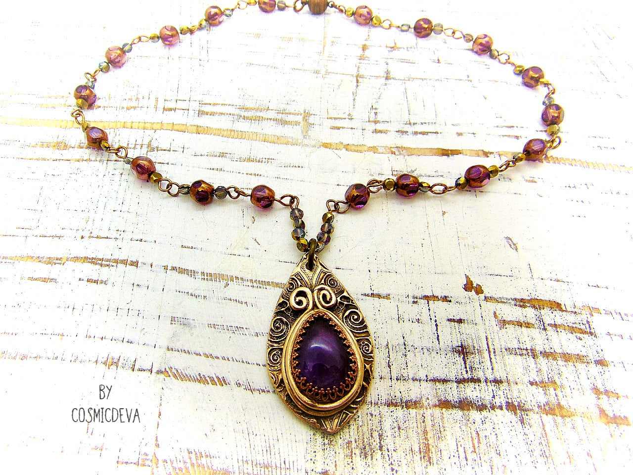 This unique Amethyst Pendant Necklace is an exquisite combination of modern and vintage. Hand sculptured in solid bronze with an elegant swirl texture and natural amethyst gemstone, its Boho gypsy style is complemented with a complete handmade rosary wire chain of purple gold faceted Czech glass beads.