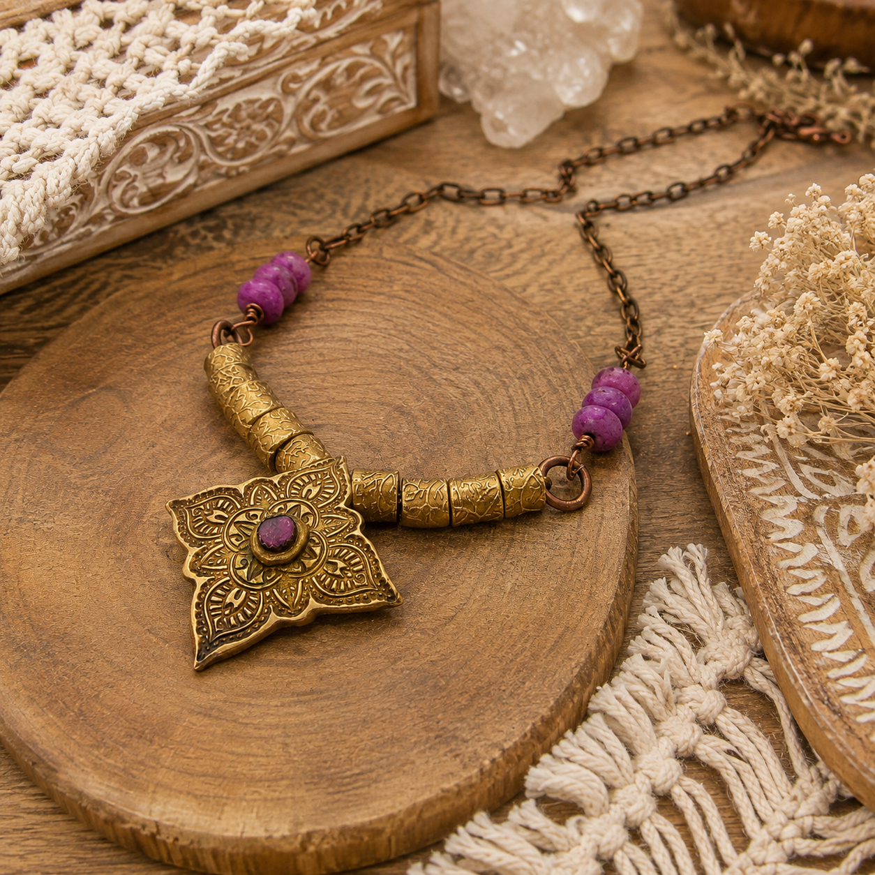 An antique-style bronze lotus pendant necklace with purple gemstone accents and cylindrical beads, displayed on a round wooden slice with bohemian props.