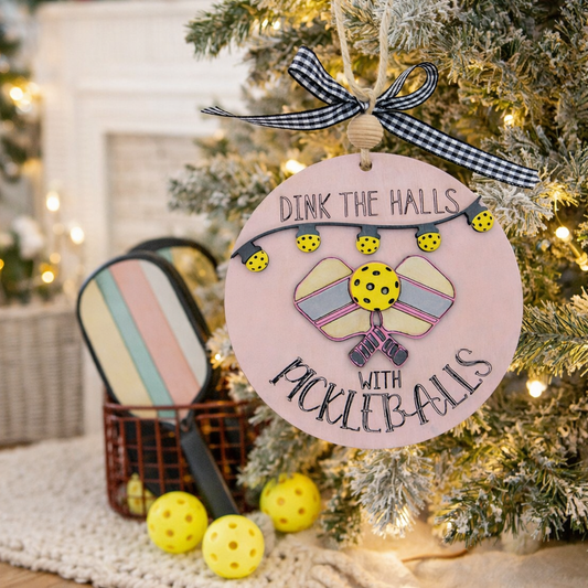 Hand painted pickleball Christmas ornament featuring the engraved phrase “Dink the Halls with Pickleballs.” Multi layered premium wood, 3D design, crossed paddles, festive garland, and handmade checkered bow. A perfect holiday gift for pickleball players and fans.