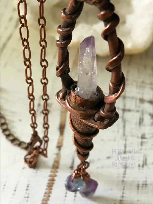 Weave a little magic into your wardrobe with this stunning magickal copper lantern necklace. Featuring a hand-sculpted, warm-glowing copper pendulum adorned with a super-clear Vera Cruz amethyst crystal point, plus two fluoride gemstones, it's a captivating conversation piece that will ignite your imagination. Suspended from an adjustable 21" copper chain, the oxidized finish and wax seal create a rich, deep warmth that will have you looking spell-bindingly beautiful. - CosmicDeva