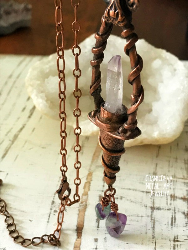 Weave a little magic into your wardrobe with this stunning magickal copper lantern necklace. Featuring a hand-sculpted, warm-glowing copper pendulum adorned with a super-clear Vera Cruz amethyst crystal point, plus two fluoride gemstones, it's a captivating conversation piece that will ignite your imagination. Suspended from an adjustable 21" copper chain, the oxidized finish and wax seal create a rich, deep warmth that will have you looking spell-bindingly beautiful.- CosmicDeva