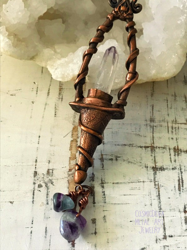 Weave a little magic into your wardrobe with this stunning magickal copper lantern necklace. Featuring a hand-sculpted, warm-glowing copper pendulum adorned with a super-clear Vera Cruz amethyst crystal point, plus two fluoride gemstones, it's a captivating conversation piece that will ignite your imagination. Suspended from an adjustable 21" copper chain, the oxidized finish and wax seal create a rich, deep warmth that will have you looking spell-bindingly beautiful.- CosmicDeva