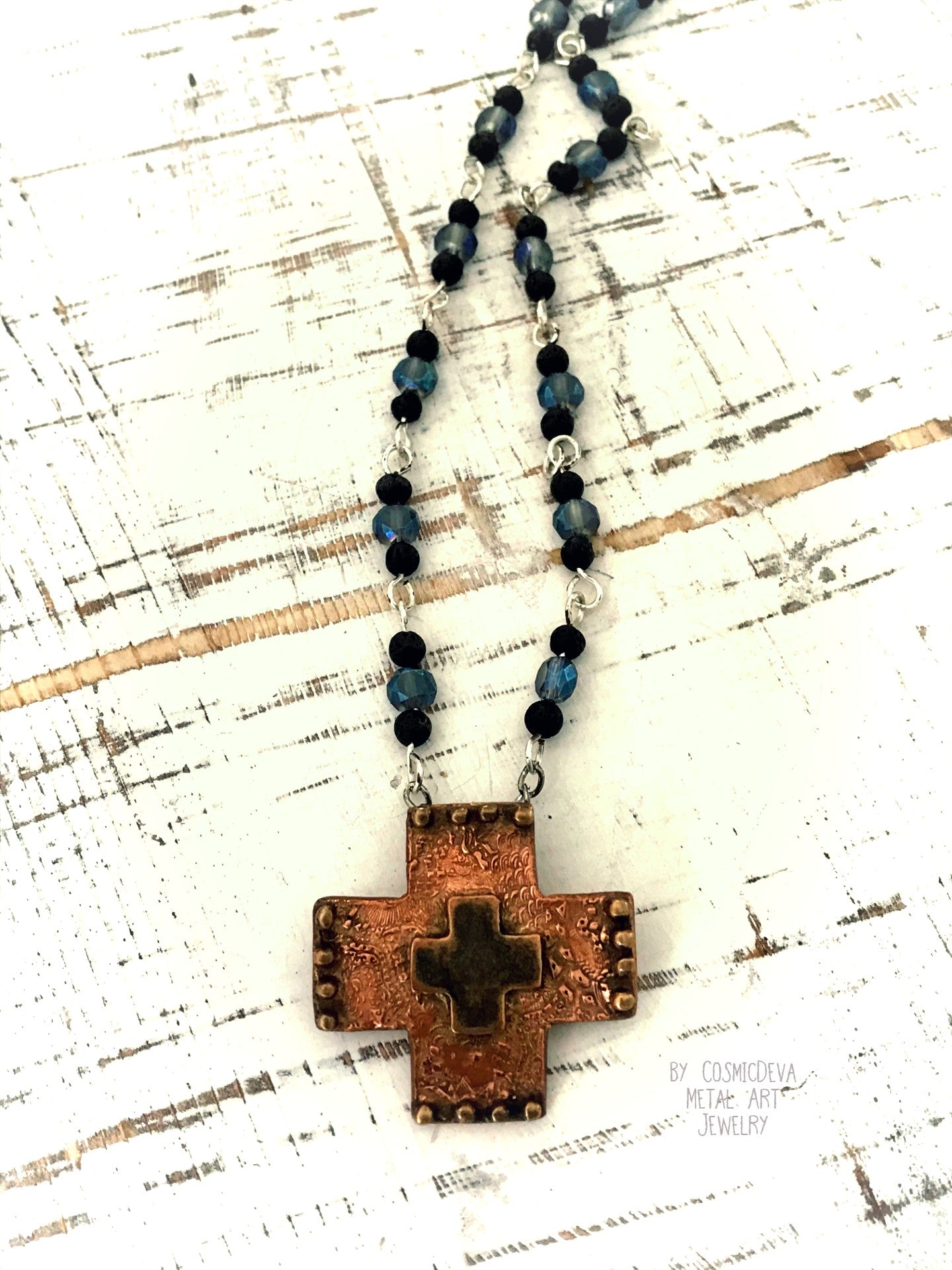 Copper Cross Rosary Necklace, Boho Faith Jewelry. A beautiful completely handmade and kiln fired western cross pendant made of solid pure copper dangles from a rosary necklace with gorgeous petite blue Czech beads and black lava beads. The handmade rosary chain is made of .925 sterling silver plated wire with sparkling blue faceted Czech glass beads and small black volcanic lava stone beads. A pretty little heart is stamped with the artist’s logo on the backside adding a lovely detail. - CosmicDeva