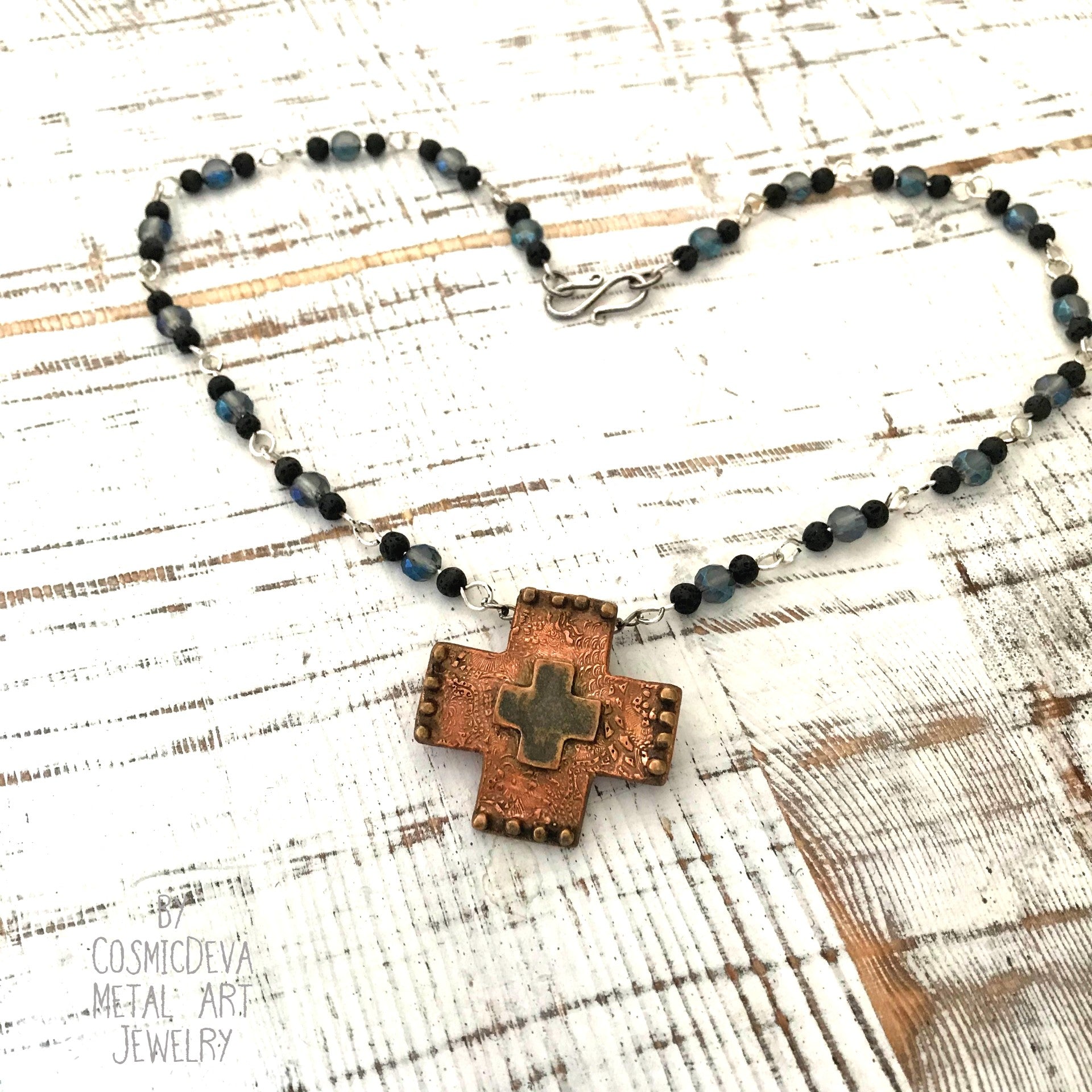 Copper Cross Rosary Necklace, Boho Faith Jewelry. A beautiful completely handmade and kiln fired western cross pendant made of solid pure copper dangles from a rosary necklace with gorgeous petite blue Czech beads and black lava beads. The handmade rosary chain is made of .925 sterling silver plated wire with sparkling blue faceted Czech glass beads and small black volcanic lava stone beads. A pretty little heart is stamped with the artist’s logo on the backside adding a lovely detail. - CosmicDeva