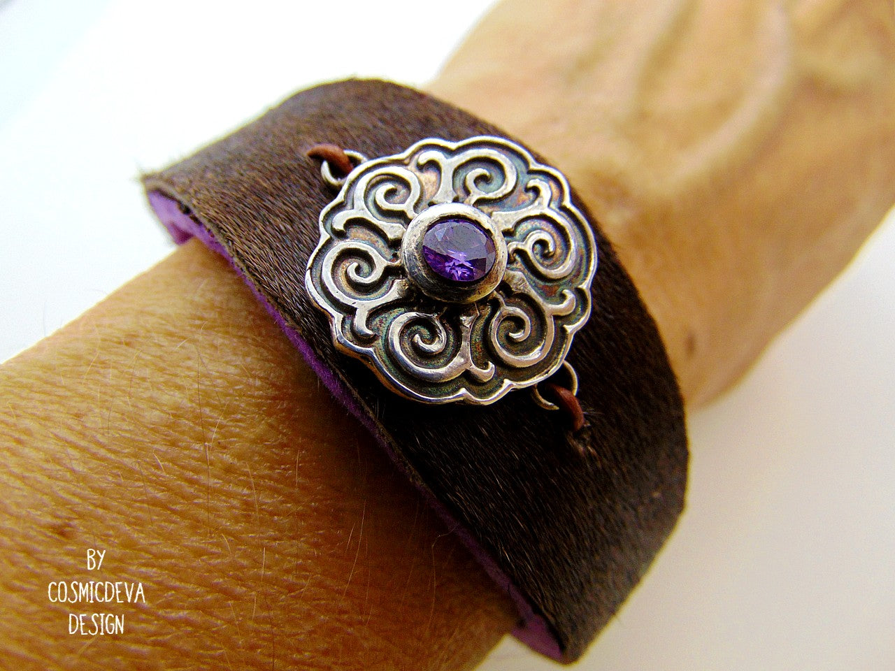 One of a kind handcrafted leather cuff bracelet made of hand cut earthy brown hair on cowhide leather. The focal point is a purple cubic zirconia amethyst in a bezel setting on a Celtic design textured solid 950 sterling silver disc. The inside of the leather bracelet is lined light purple/ lilac felt for your comfort. The handmade bracelet has silver colored stainless steel magnetic clasp which makes it easy to open and close.