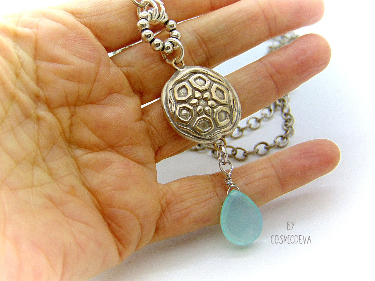 Beautiful handmade silver bronze lentil pendant with a mandala texture and a large faceted briolette aqua blue chalcedony gemstone dangle bead. The large hand formed lentil bead is double sided with two different designs and so can be worn facing either side.  The pendant suspends from an 18 inch – 20-inch-long chain with accentual faceted Brazilian aquamarine abacus beads and Tibetan silver beads.