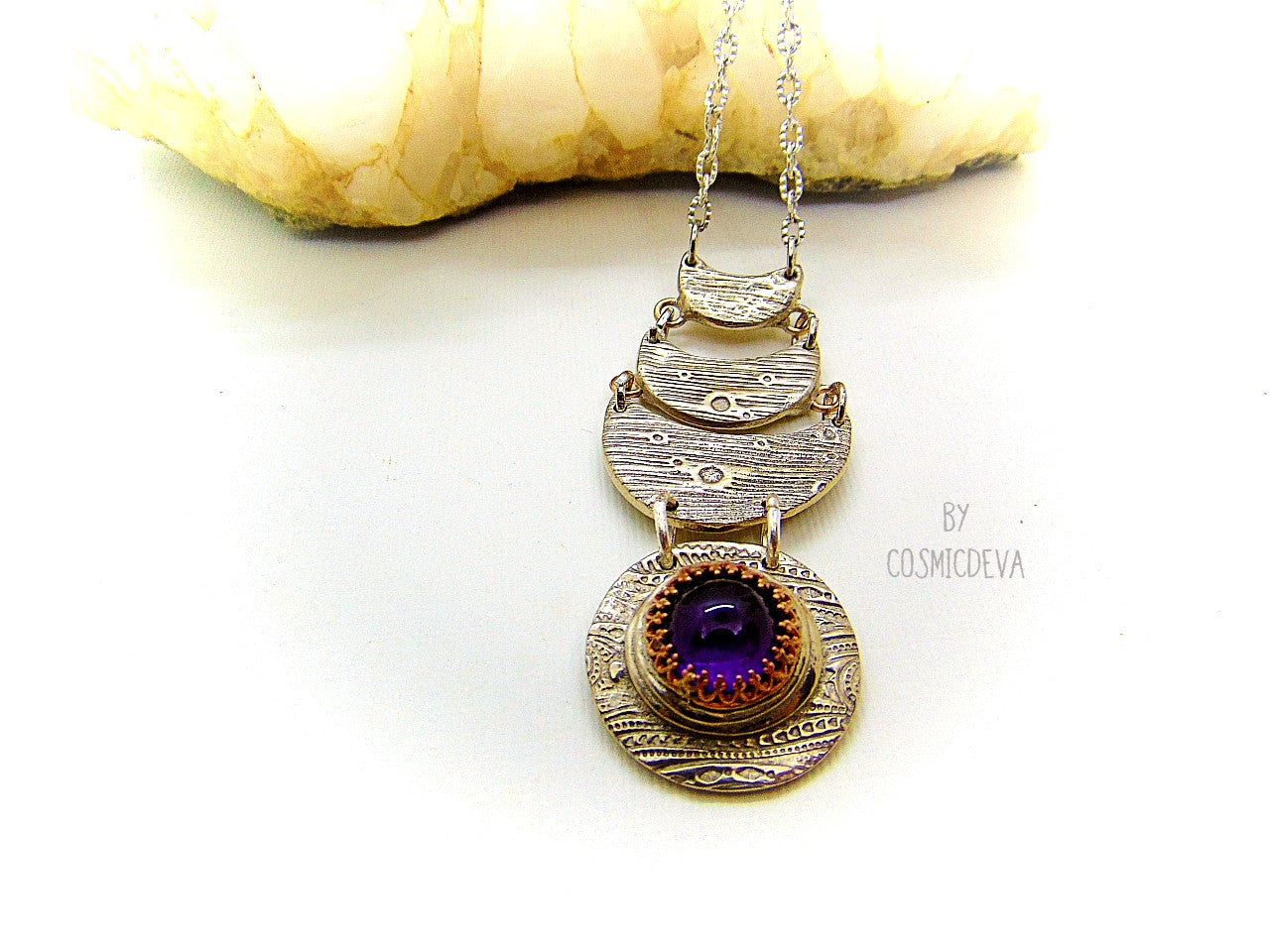 Beautiful purple silver moon phase necklace with a natural amethyst cabochon as a focal point. This silver bronze crescent moon pendant was completely hand formed and kiln fired. Silver bronze has the look of sterling silver but for a more affordable price. The moon pendant suspends from an 18 inch – 20-inch-long chain.