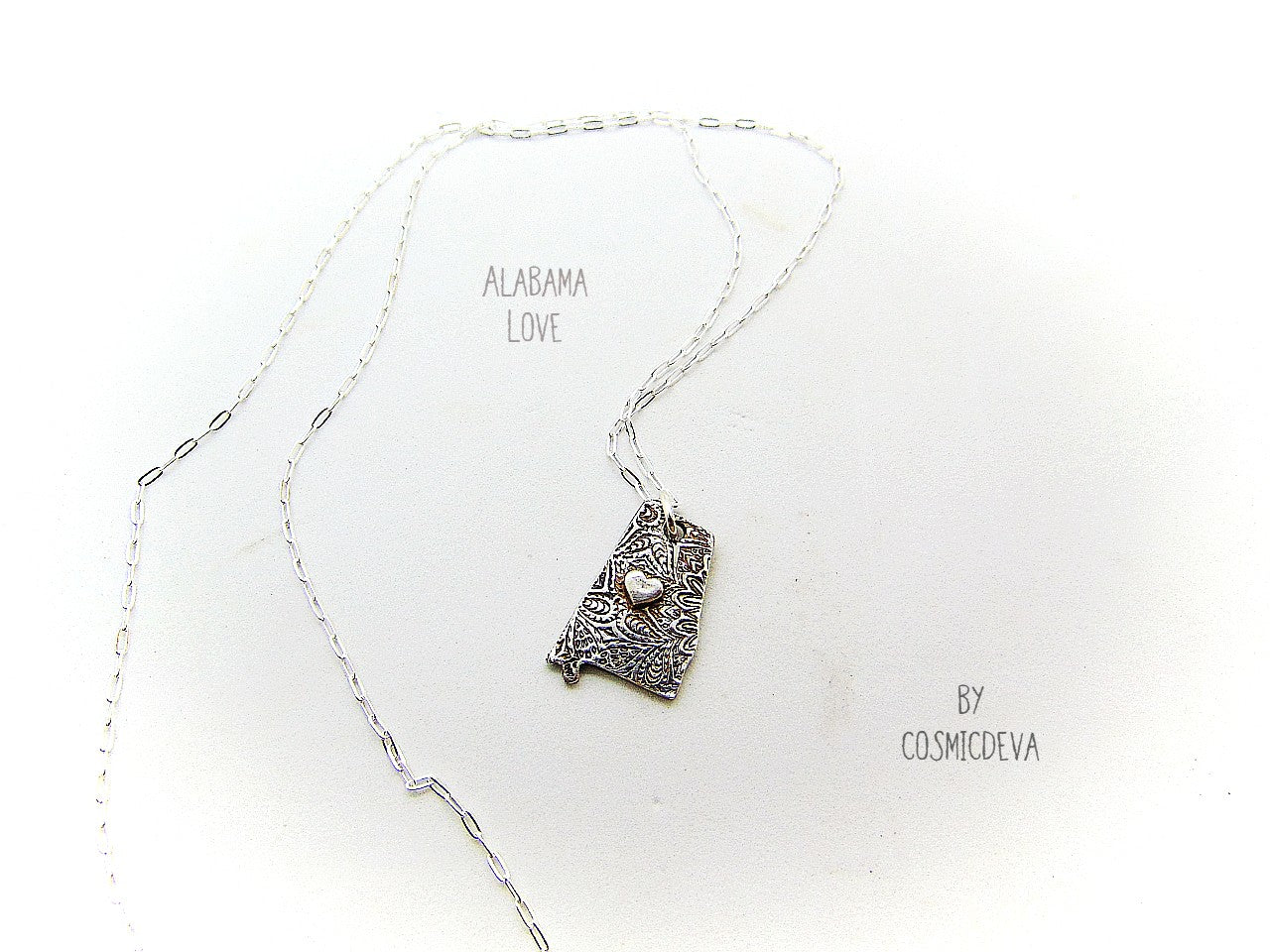 Shine your love for Alabama with this stunningly handcrafted and kiln-fired sterling silver necklace, featuring a delicate Alabama-shaped pendant with a heart in the center. Show off your state pride with a unique and fashionable piece of jewelry that is hallmarked as sterling silver and signed by CosmicDeva. Alabama love never looked so beautiful!