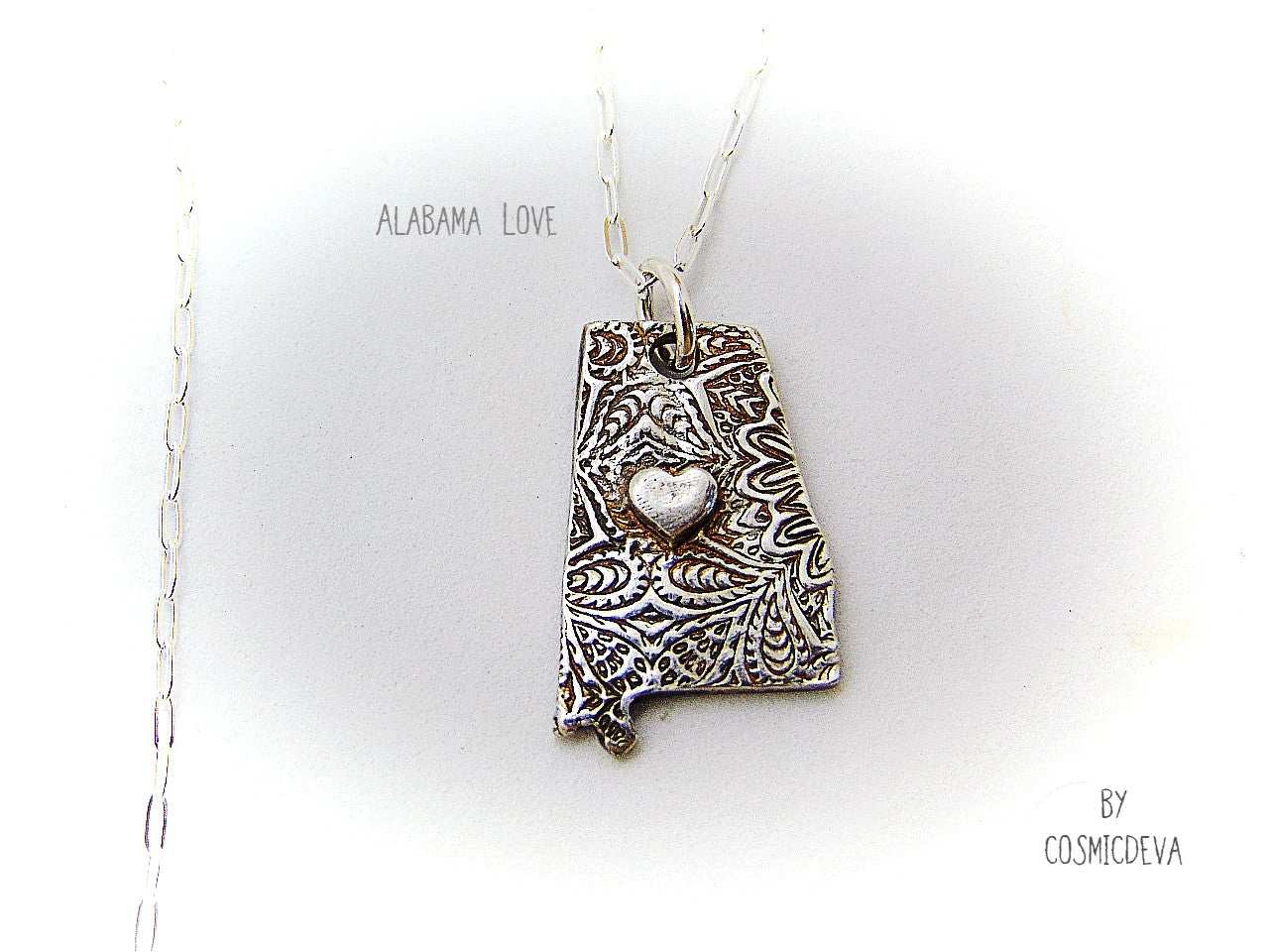 Shine your love for Alabama with this stunningly handcrafted and kiln-fired sterling silver necklace, featuring a delicate Alabama-shaped pendant with a heart in the center. Show off your state pride with a unique and fashionable piece of jewelry that is hallmarked as sterling silver and signed by CosmicDeva. Alabama love never looked so beautiful!