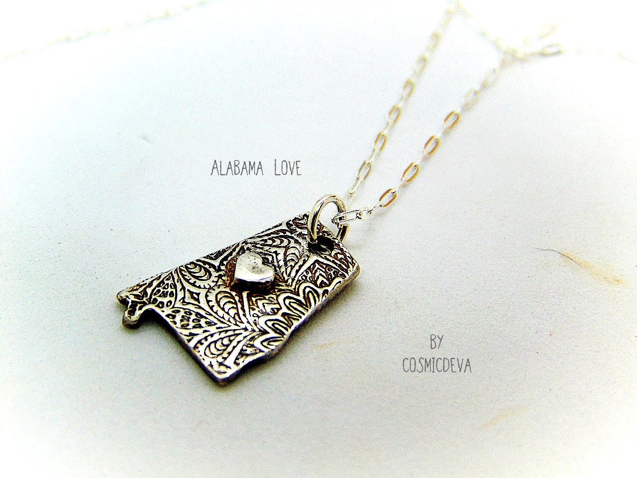 Shine your love for Alabama with this stunningly handcrafted and kiln-fired sterling silver necklace, featuring a delicate Alabama-shaped pendant with a heart in the center. Show off your state pride with a unique and fashionable piece of jewelry that is hallmarked as sterling silver and signed by CosmicDeva. Alabama love never looked so beautiful!