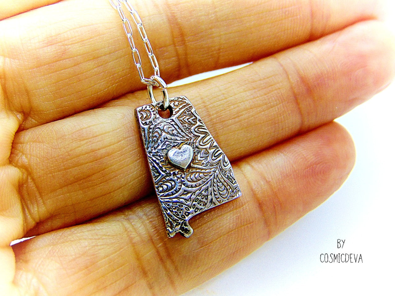 Shine your love for Alabama with this stunningly handcrafted and kiln-fired sterling silver necklace, featuring a delicate Alabama-shaped pendant with a heart in the center. Show off your state pride with a unique and fashionable piece of jewelry that is hallmarked as sterling silver and signed by CosmicDeva. Alabama love never looked so beautiful!