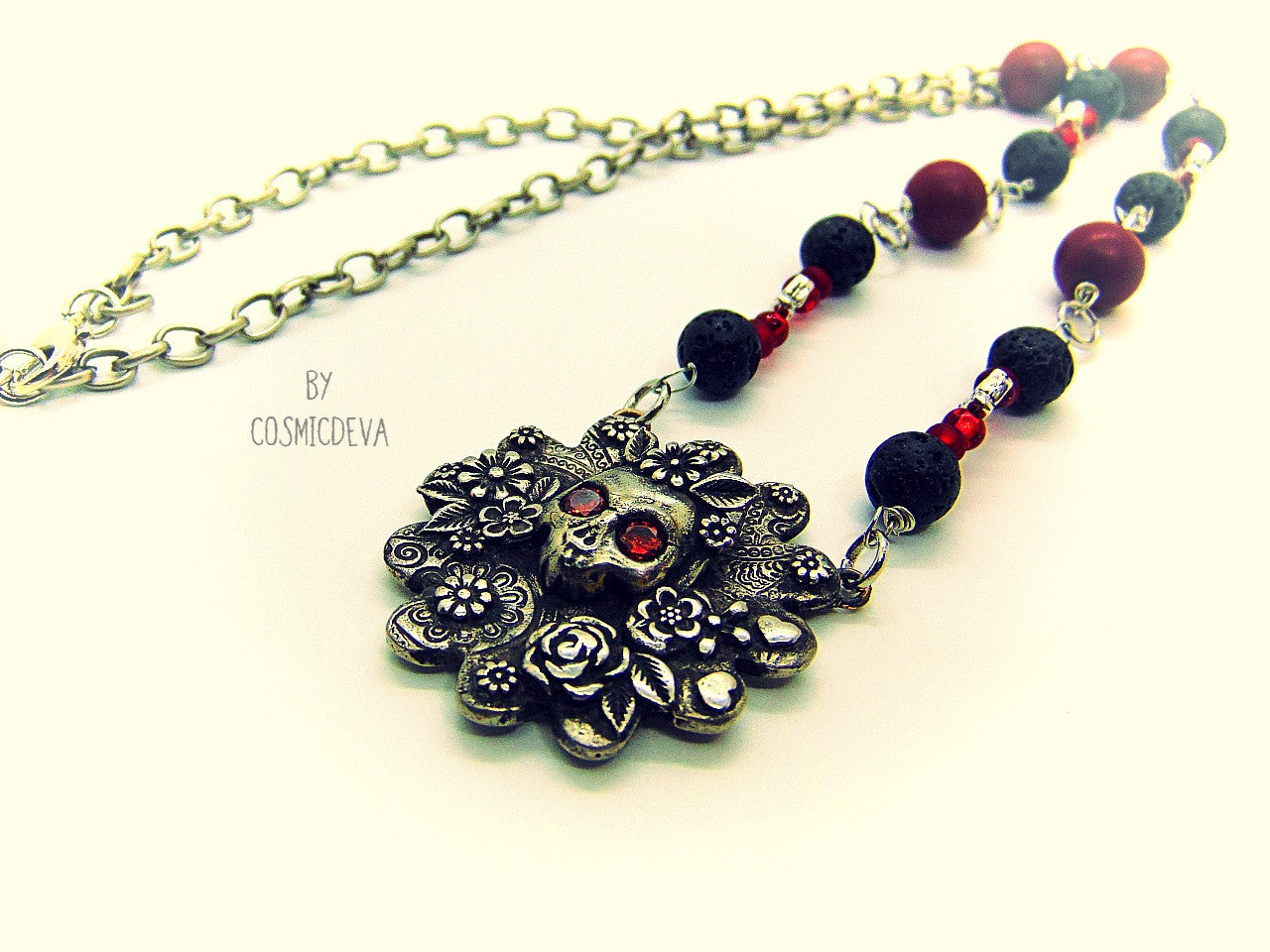 Unique detailed silver bronze Frida Kahlo sugar skull pendant necklace influenced by Mexican culture and symbolism. The flower shaped 3d pendant is featuring a sugar skull decorated with the typical Frida Kahlo signature floral wreath and faceted red garnet cubic zirconia gemstones as eyes. Incorporated flowers, roses, leaves and tiny hearts surrounding the skull. On the backside of the pendant is the CosmicDeva Hallmark