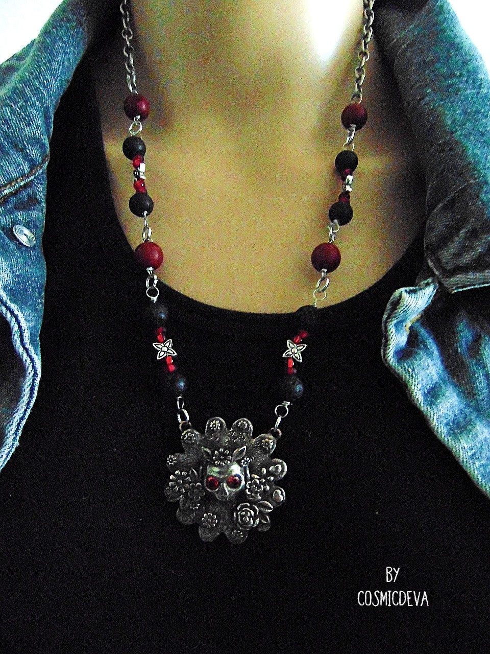 Unique detailed silver bronze Frida Kahlo sugar skull pendant necklace influenced by Mexican culture and symbolism. The flower shaped 3d pendant is featuring a sugar skull decorated with the typical Frida Kahlo signature floral wreath and faceted red garnet cubic zirconia gemstones as eyes. Incorporated flowers, roses, leaves and tiny hearts surrounding the skull. On the backside of the pendant is the CosmicDeva Hallmark