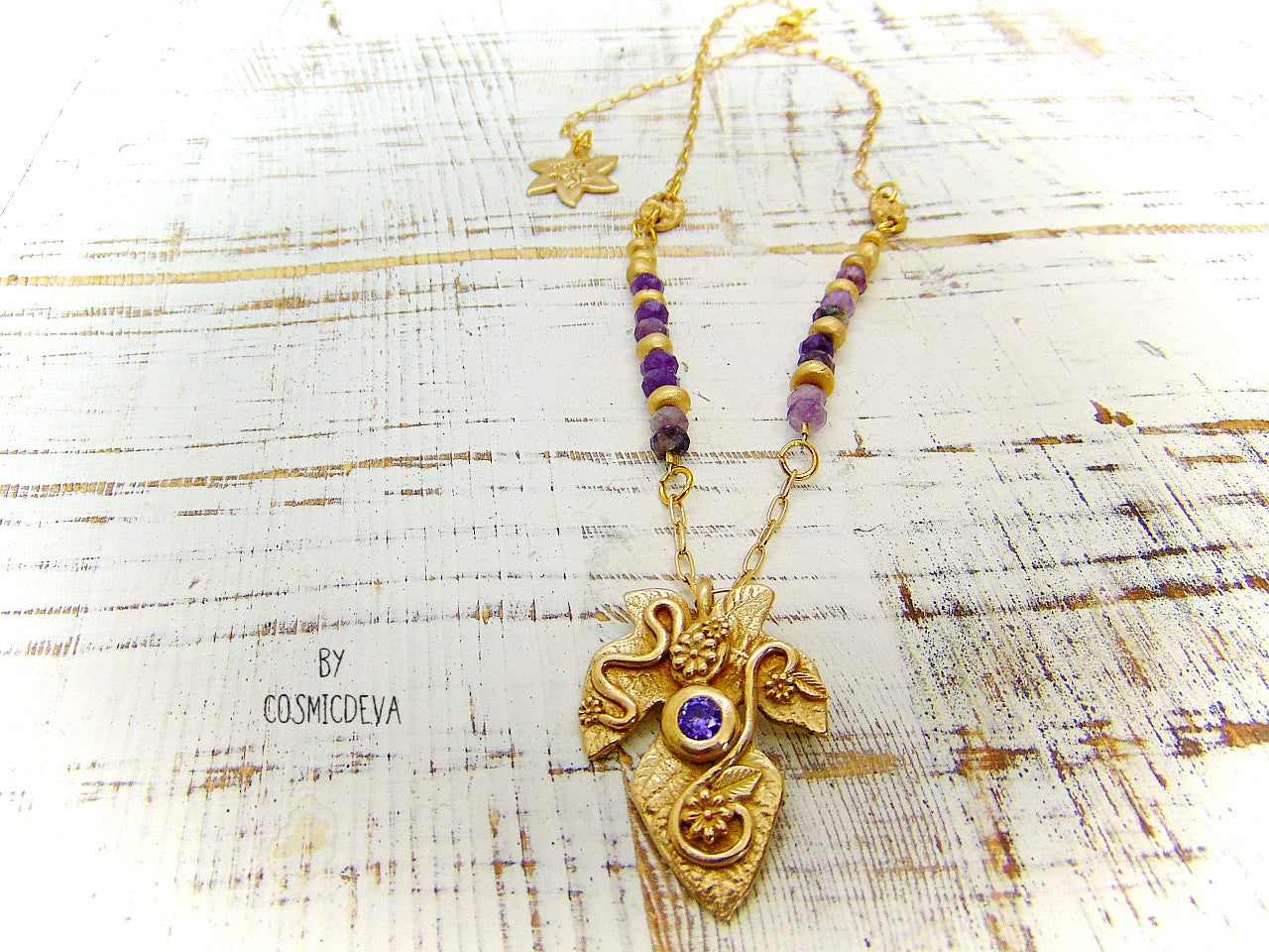 Playful handcrafted fig leaf with an Amethyst in the center and adorned with flowers and swirls. The dainty 18–21-inch necklace is strung with small facetted raw natural lepidolite gemstone rondelle beads and hand formed gold bronze pearls and connectors. I created and casted this leaf with a small fig tree leaf from our garden.