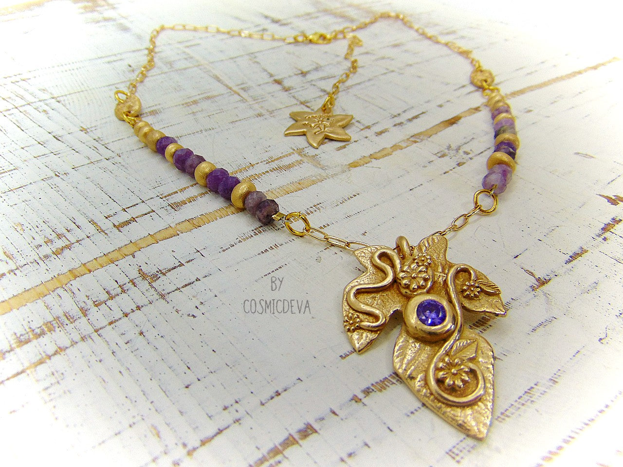 Playful handcrafted fig leaf with an Amethyst in the center and adorned with flowers and swirls. The dainty 18–21-inch necklace is strung with small facetted raw natural lepidolite gemstone rondelle beads and hand formed gold bronze pearls and connectors. I created and casted this leaf with a small fig tree leaf from our garden.