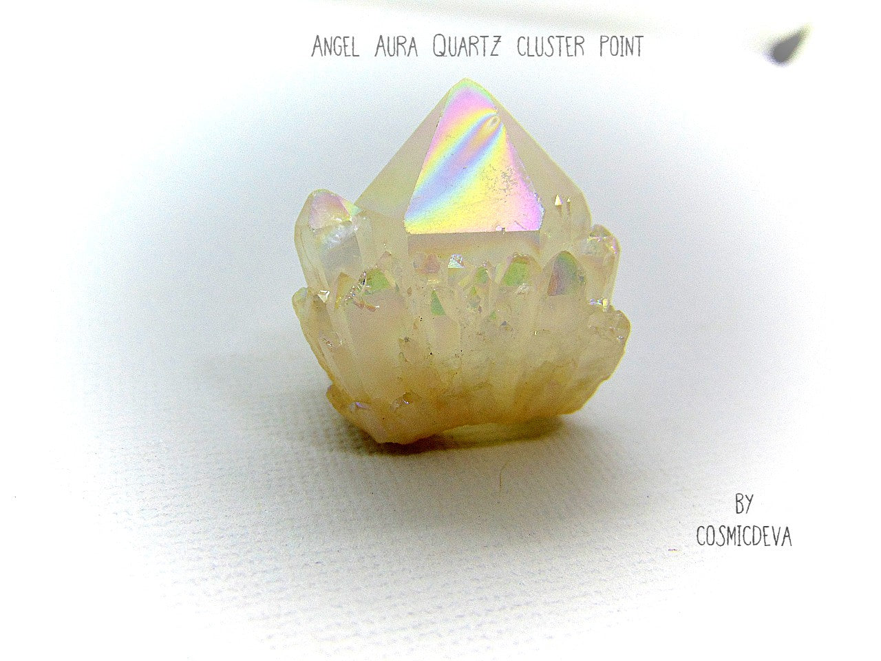 This outstanding shimmering iridescence Angel Aura Quartz crystal point is surrounded with many small crystal clusters around its base. Angel Aura Quartz is natural clear quartz with an infusion of pure titanium, silver and gold. The Natural Clear Quartz Point is placed in a pressurized chamber at high temperature and exposed to pure vaporized precious metal. 