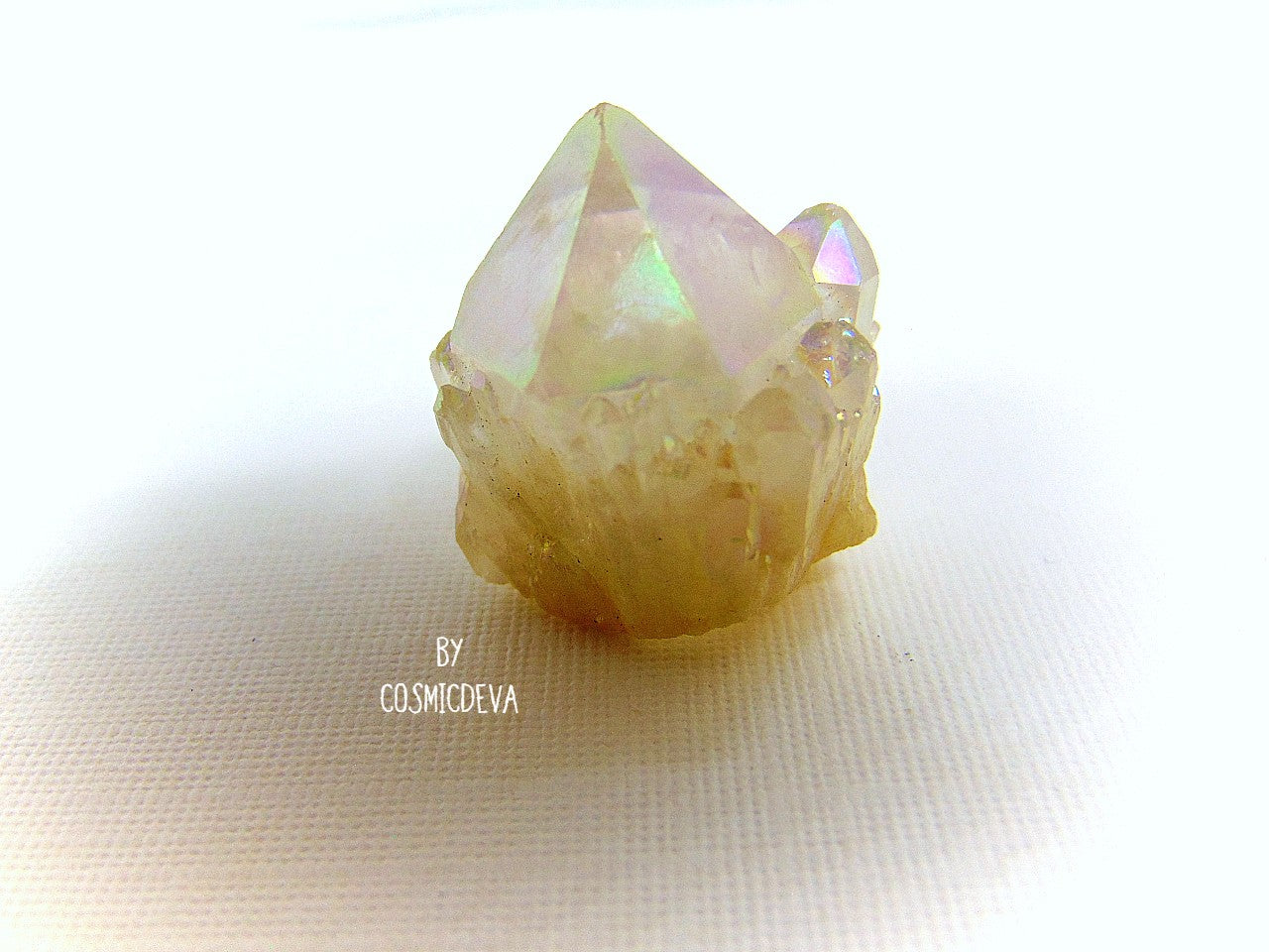 This outstanding shimmering iridescence Angel Aura Quartz crystal point is surrounded with many small crystal clusters around its base. Angel Aura Quartz is natural clear quartz with an infusion of pure titanium, silver and gold. The Natural Clear Quartz Point is placed in a pressurized chamber at high temperature and exposed to pure vaporized precious metal. 