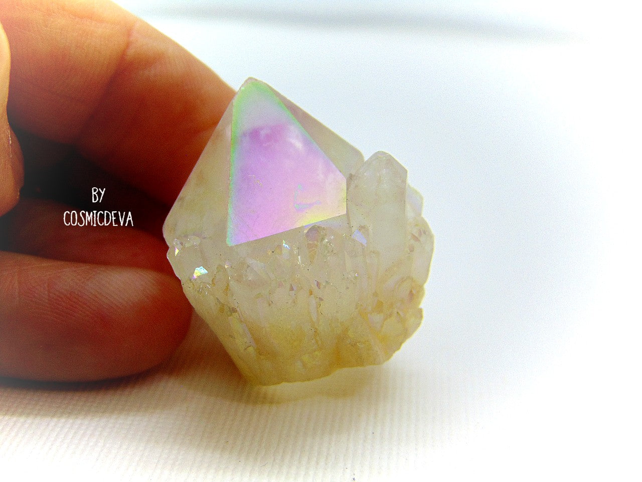 This outstanding shimmering iridescence Angel Aura Quartz crystal point is surrounded with many small crystal clusters around its base. Angel Aura Quartz is natural clear quartz with an infusion of pure titanium, silver and gold. The Natural Clear Quartz Point is placed in a pressurized chamber at high temperature and exposed to pure vaporized precious metal. 